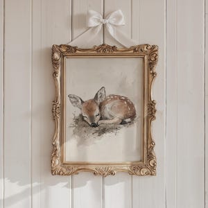 May include: A framed watercolour painting of a sleeping fawn with brown and white fur. The frame is gold with ornate details.