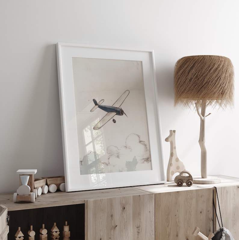 May include: A framed print of a vintage airplane in flight, with a blue and white color scheme. The artwork is displayed on a wooden cabinet, alongside a wooden giraffe, car, and a tree-shaped lamp with a textured lampshade. The scene evokes a nursery or children's room.
