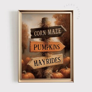 May include: Framed autumn-themed print featuring a wooden signpost with directional arrows. The arrows point to "Corn Maze," "Pumpkins," and "Hayrides." The artwork has a warm color palette with pumpkins at the base.