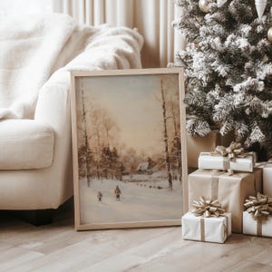 Puede incluir: Pintura enmarcada de un paisaje invernal con un marco de madera clara. La obra representa una escena nevada con figuras caminando por un bosque. La pintura est&aacute; apoyada contra un sof&aacute; blanco. Regalos envueltos con lazos dorados est&aacute;n junto a un &aacute;rbol de Navidad.
