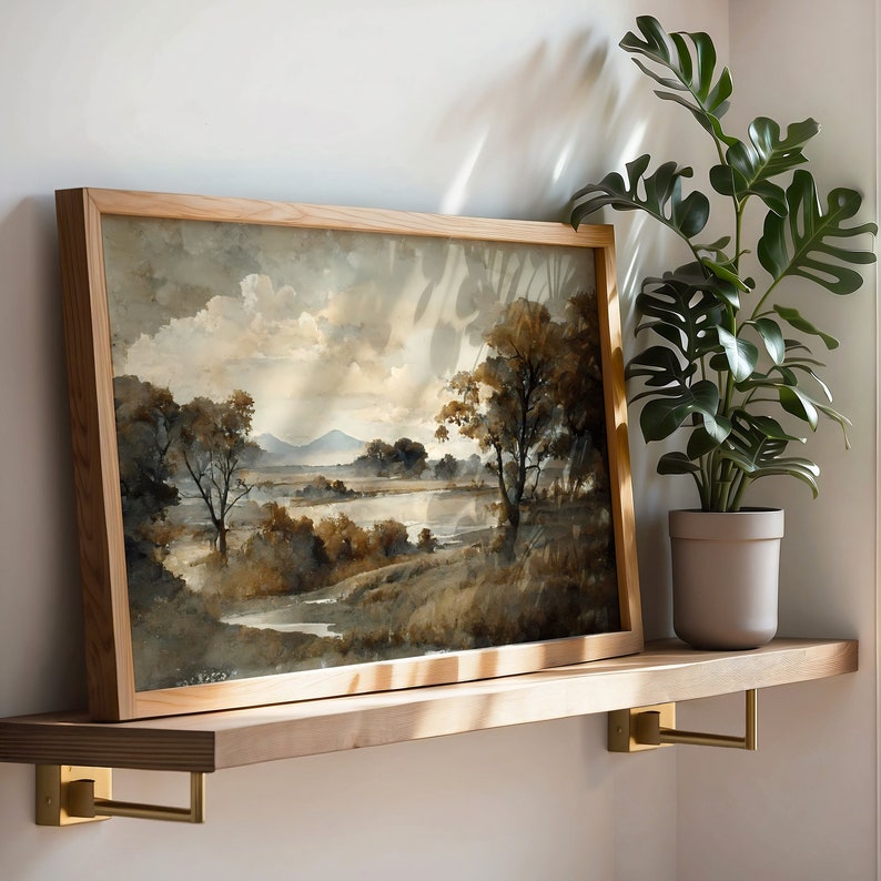 May include: A framed watercolor painting of a landscape with trees, hills, and a river. The painting is in a wooden frame and is hanging on a wall.