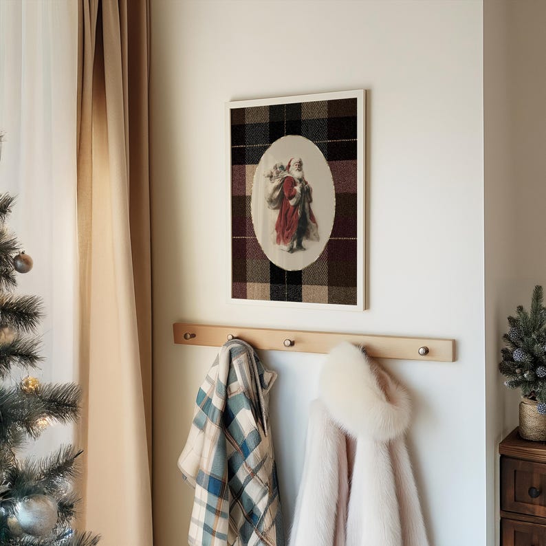 May include: A framed print of Santa Claus in a red coat and white beard, set against a plaid background. Below, a wooden coat rack holds a plaid blanket and a pink coat with a fur-trimmed hood. A Christmas tree is visible on the left.