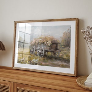May include: A framed painting of a wooden wagon filled with pink and white flowers, set against a soft, hazy background of a field and trees.