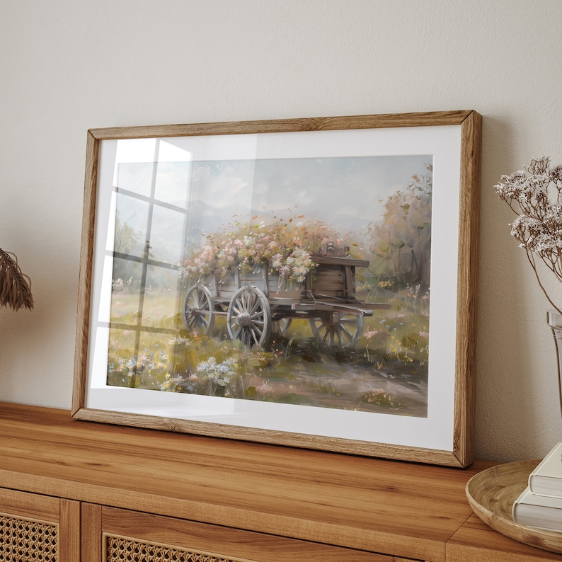 May include: A framed painting of a wooden wagon filled with pink and white flowers, set against a soft, hazy background of a field and trees.