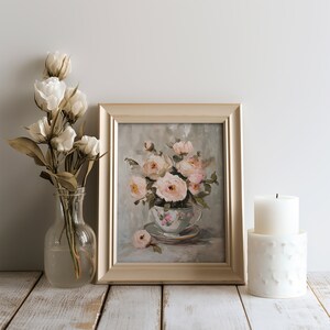 May include: A framed painting of a bouquet of pink roses in a vintage teacup. The painting is on a whitewashed wooden surface with a white candle and a vase of white flowers.