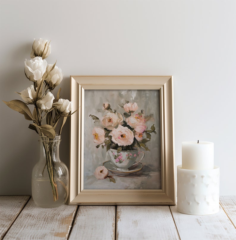 May include: A framed painting of a bouquet of pink roses in a vintage teacup. The painting is on a whitewashed wooden surface with a white candle and a vase of white flowers.