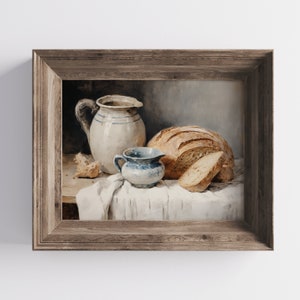 Peut inclure: Peinture encadr&eacute;e repr&eacute;sentant une nature morte avec un pain, une petite cruche bleue et blanche, et une grande cruche blanche &agrave; rayures bleues. Un morceau de pain est cass&eacute;. La peinture est de style rustique.