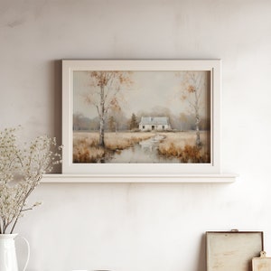 May include: A framed painting of a white cottage in a field with a stream running through it. The cottage has a gray roof and is surrounded by trees. The painting is in a white frame and is hanging on a white wall.