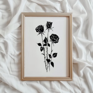 May include: A black and white print of three black roses in a simple silhouette style. The roses are arranged in a bouquet with stems and leaves. The print is framed in a light wood frame.