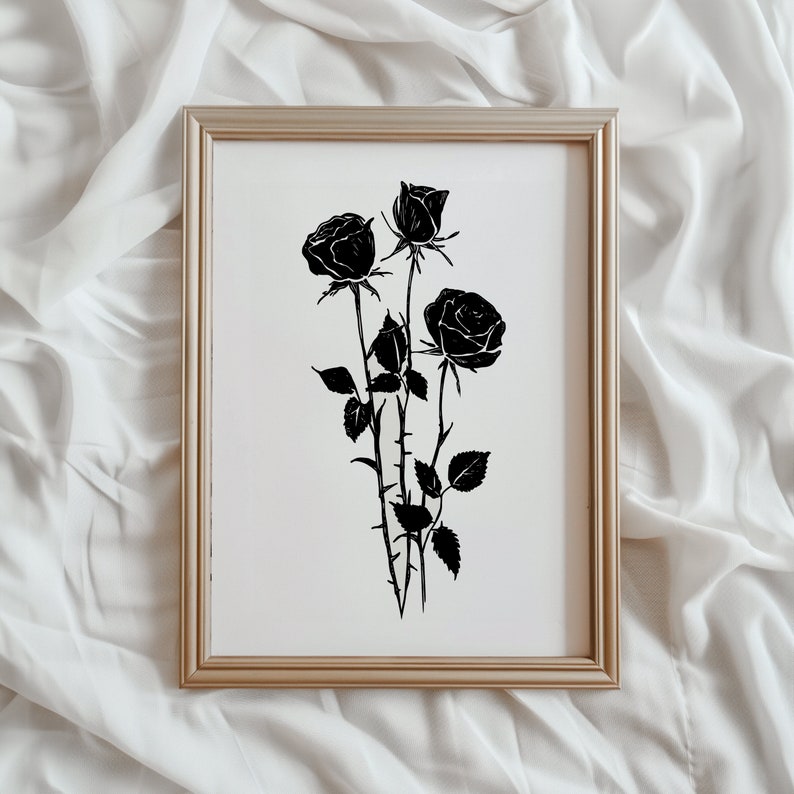 May include: A black and white print of three black roses in a simple silhouette style. The roses are arranged in a bouquet with stems and leaves. The print is framed in a light wood frame.