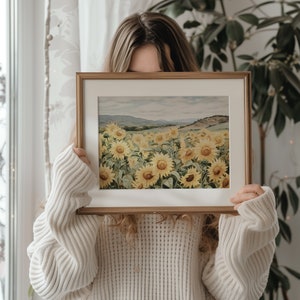 May include: A framed watercolour painting of a field of sunflowers in a landscape setting. The sunflowers are yellow with green leaves and stems. The background is a light blue sky with a distant mountain range.