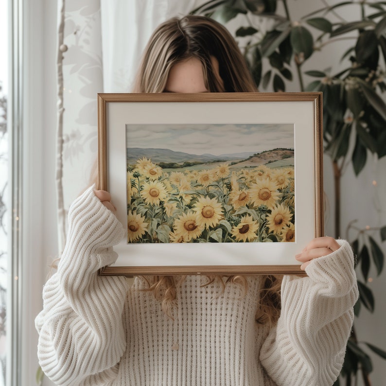 May include: A framed watercolour painting of a field of sunflowers in a landscape setting. The sunflowers are yellow with green leaves and stems. The background is a light blue sky with a distant mountain range.