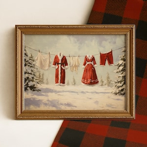 May include: A framed painting depicts a snowy winter scene with clothes hanging on a clothesline. The clothes include a red robe, dress, and shorts, all with white trim, and white undergarments. The painting is in a gold frame.