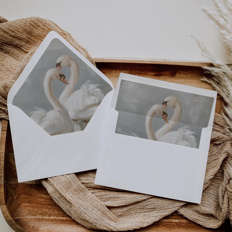May include: Two white swans with their necks intertwined, a romantic image printed on a white card with a light blue background. The card is inside a white envelope.