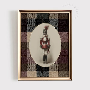 Puede incluir: Una impresión enmarcada con una ilustración vintage de un soldado cascanueces. El cascanueces viste un uniforme rojo con sombrero y botas negras, sobre un fondo a cuadros en tonos marrón, negro y rojo. El marco es dorado y la impresión tiene el texto "FAERY PRINTS".