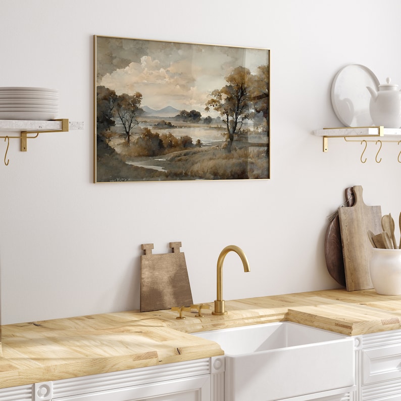 May include: A framed watercolor painting of a landscape with trees, a lake, and mountains in the background. The painting is in shades of brown, gray, and white.