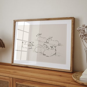 May include: A framed black and white line drawing of a group of lambs lying down in a field. The frame is made of wood and has a light brown finish.