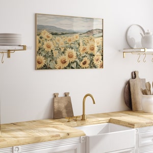 May include: A framed watercolour painting of a field of sunflowers in a landscape setting. The sunflowers are yellow with green leaves and the background is a light blue sky with a few clouds. The painting is framed in a gold frame.