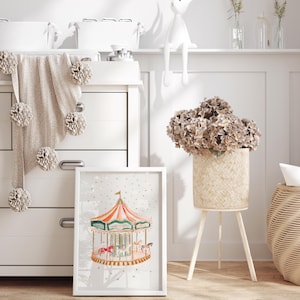 May include: A white framed print of a colourful carousel with gold accents. The print is hanging on a white wall in a nursery. A wicker basket with dried flowers sits on a wooden stand in the foreground.