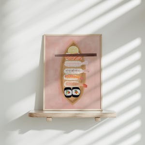 May include: A framed illustration of a pink background with a wooden boat filled with sushi. The boat contains shrimp, avocado, and cucumber sushi rolls, as well as two maki rolls. A lemon wedge is visible in the boat. Two chopsticks are placed on top of the boat.