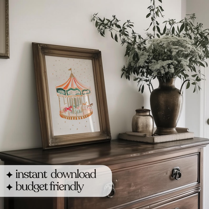 May include: A framed print of a colourful carousel with a white background and gold stars. The print is hanging on a wall above a wooden dresser with drawers.