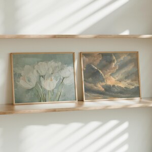 May include: Two framed art prints on a wooden shelf. One print features white tulips against a light blue background. The other depicts a dramatic cloudscape with shades of gray, brown, and yellow.