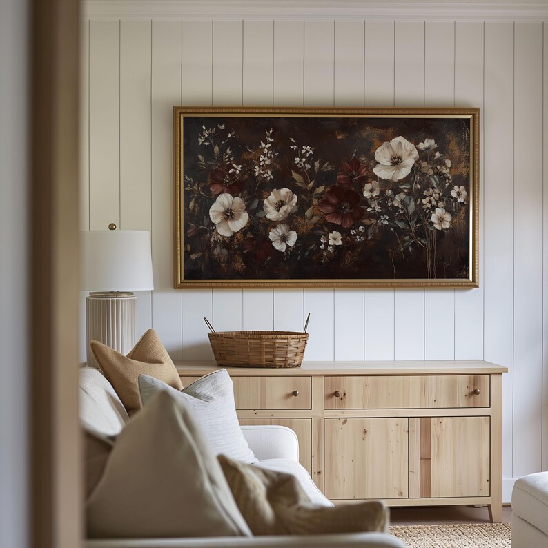 May include: A living room with a white couch, a wooden cabinet, and a framed floral painting on the wall. The couch has a few pillows and a basket is on top of the cabinet.