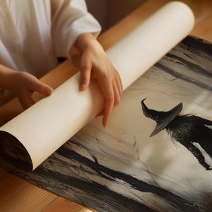 May include: A black and white illustration of a witch with a pointed hat and long flowing robes, printed on a white canvas. The canvas is being rolled up by a person's hand.