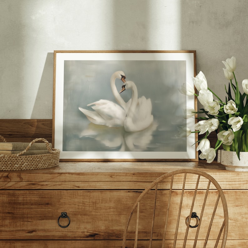 May include: A framed print of two white swans with their necks intertwined in a heart shape, set against a soft blue background. The swans are reflected in the water below.