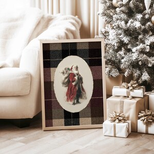 May include: A framed Christmas print featuring Santa Claus carrying a sack. The image of Santa is set in an oval frame against a plaid background of black, brown, and beige. The print is displayed near a Christmas tree and wrapped gifts.