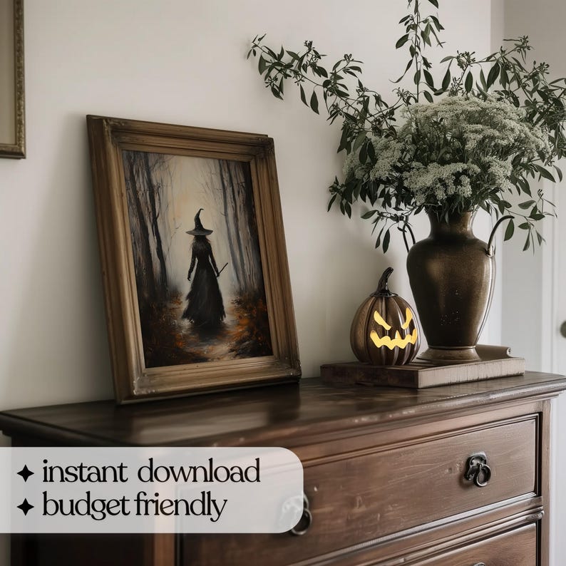 May include: A framed painting of a witch walking through a dark forest. The painting is on a wooden dresser with a lit jack-o'-lantern and a vase of white flowers.