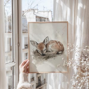 May include: A framed watercolour painting of a fawn sleeping on a bed of leaves. The fawn is brown with white spots and has its eyes closed. The painting is set against a white background.