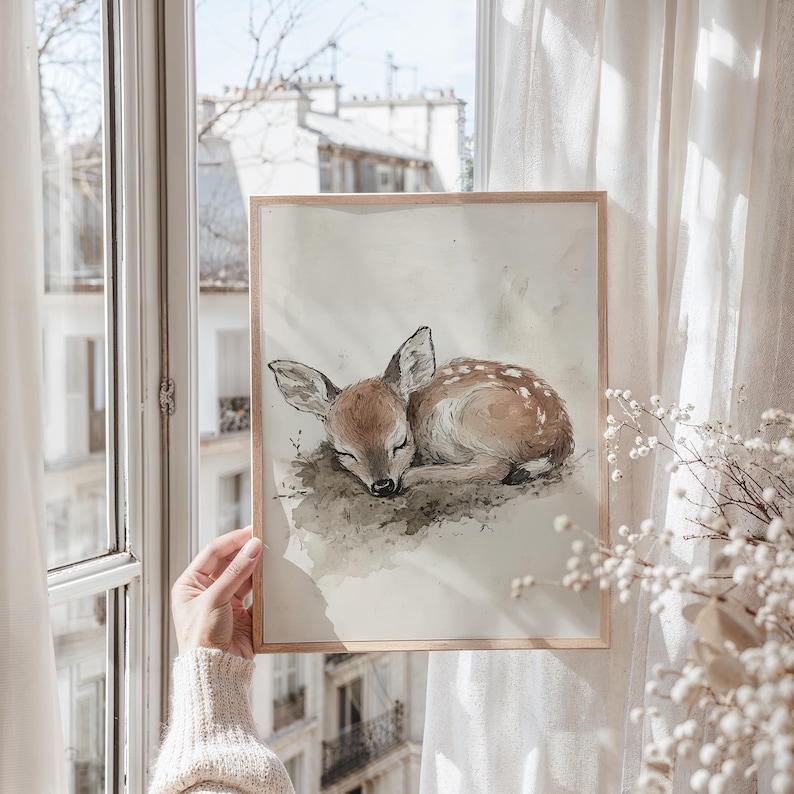 May include: A framed watercolour painting of a fawn sleeping on a bed of leaves. The fawn is brown with white spots and has its eyes closed. The painting is set against a white background.