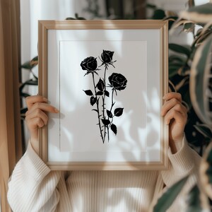 May include: A framed print of a black and white silhouette of three roses with stems and leaves.