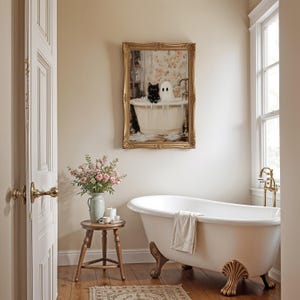 May include: A white clawfoot bathtub with a towel draped over the edge, a small wooden stool with a vase of pink flowers, and a framed painting of a black cat and a white ghost in a bathtub. The painting is in a gold frame and has a floral background.