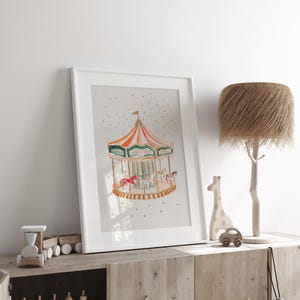 May include: A white framed print of a watercolour painting of a carousel with a red, orange and green striped canopy. The carousel is surrounded by gold stars on a light grey background.