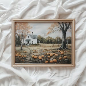 Puede incluir: Una pintura enmarcada que representa una casa de campo blanca con un techo marrón, rodeada de árboles y un campo de calabazas. La pintura está en un marco de madera claro.