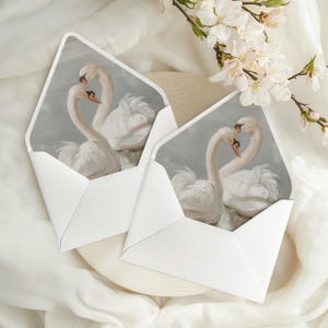 May include: Two white swans with their necks intertwined, painted in a soft, romantic style on a grey background. The image is printed on a white envelope.