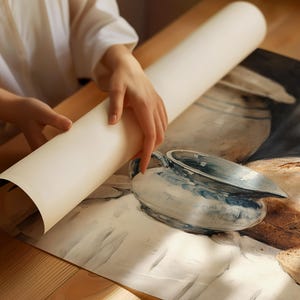 Peut inclure: Un rouleau de papier cr&egrave;me en cours de d&eacute;roulement, r&eacute;v&eacute;lant une peinture de nature morte avec une cruche bleue et blanche et du pain. L'impression est sur une surface en bois.