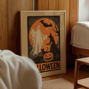 K&ouml;nnte beinhalten: Gerahmtes Halloween-Poster mit einem Geist, einer Hexe, einer schwarzen Katze und einem K&uuml;rbis vor einem orangefarbenen Mond. Das Wort "HALLOWEEN" ist unten in Orange gedruckt. Das Kunstwerk befindet sich in einem Holzrahmen und lehnt an einer Holzwand.
