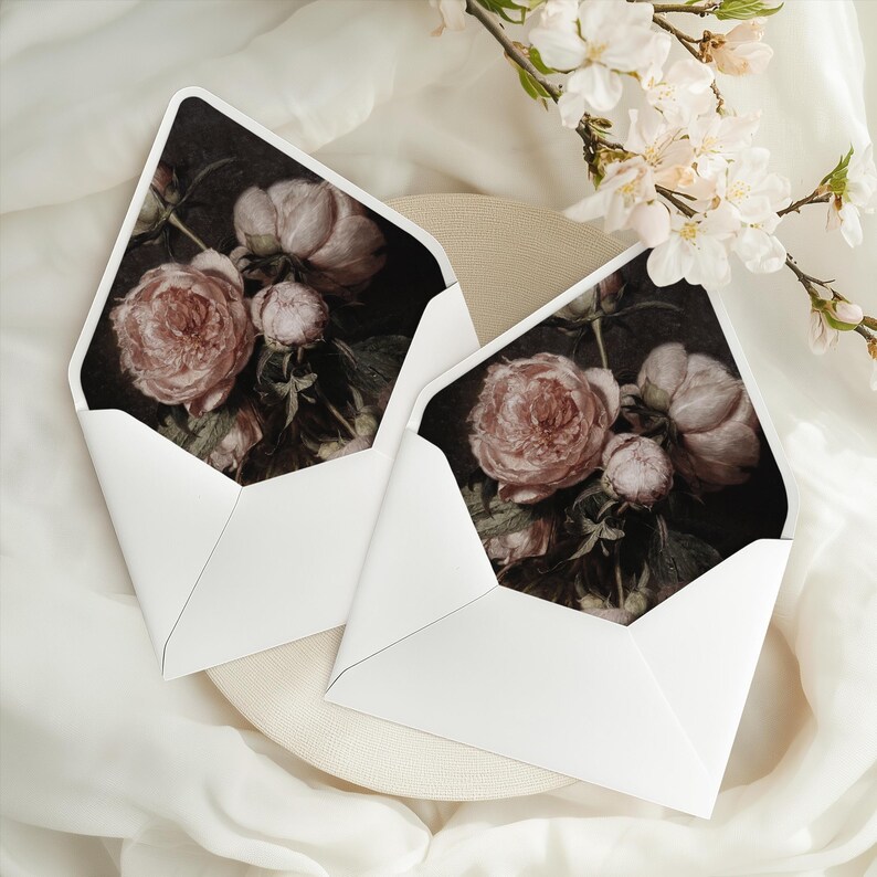 May include: Two white envelopes with a dark background floral design featuring pink roses. The envelopes are on a white surface.