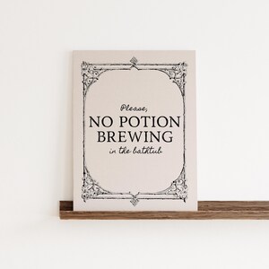 May include: A rectangular sign with a cream background and black text that reads "Please, NO POTION BREWING in the bathtub." The sign has a decorative black border and is displayed on a wooden shelf.