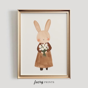 May include: A brown bunny rabbit with a brown dress and white flowers in its paws. The bunny is standing on a white background. The image is framed in a gold frame.