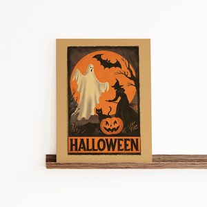 K&ouml;nnte beinhalten: Ein Halloween-Poster mit einem Geist, einer Hexe, einer schwarzen Katze und einem K&uuml;rbis vor einem orangefarbenen Mond. Das Wort "HALLOWEEN" wird unten in fetter, orangefarbener Schrift angezeigt. Das Poster ist in einem braunen Rahmen eingefasst.