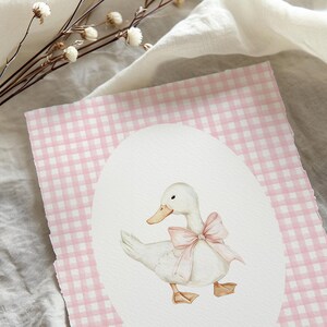 Puede incluir: Una ilustraci&oacute;n de acuarela de un pato blanco con un lazo rosa sobre un fondo de cuadros vichy rosa y blanco.