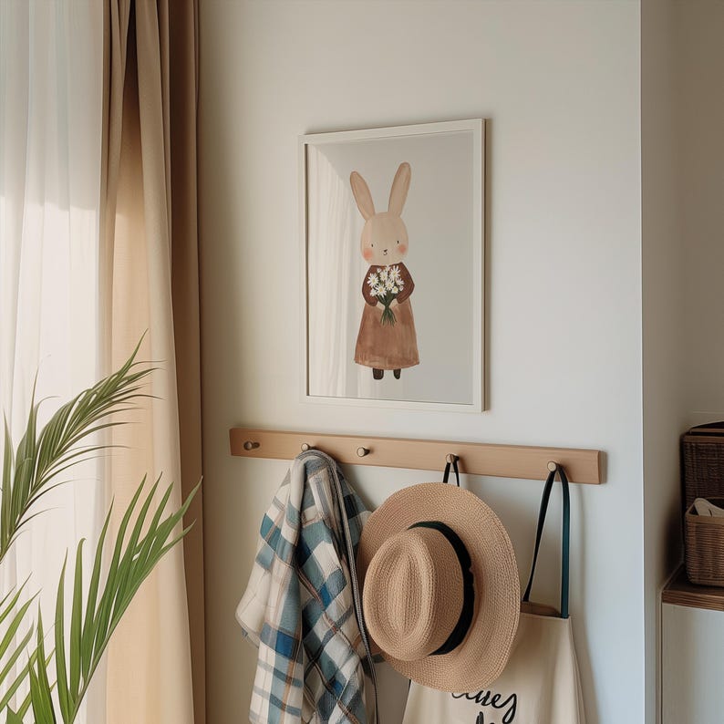 May include: A framed illustration of a brown rabbit holding a bouquet of white flowers. The rabbit is wearing a brown dress and is standing on a white background. The frame is white and has a simple design.