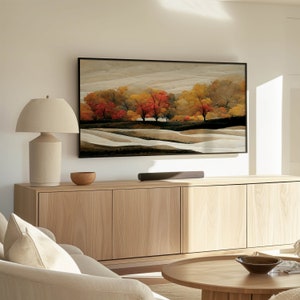 Puede incluir: Un armario de madera clara con tres puertas y una barra de sonido debajo. Una l&aacute;mpara con una pantalla beige se encuentra a la izquierda del armario. Una pintura enmarcada de un paisaje con &aacute;rboles en colores oto&ntilde;ales cuelga sobre el armario.