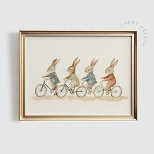 Op de afbeelding: Een ingelijste print met vier antropomorfe konijnen op fietsen. De konijnen dragen verschillende outfits. Het kunstwerk is in aquarel stijl, tegen een neutrale achtergrond en goudkleurig omlijst. Kinderlijk thema.