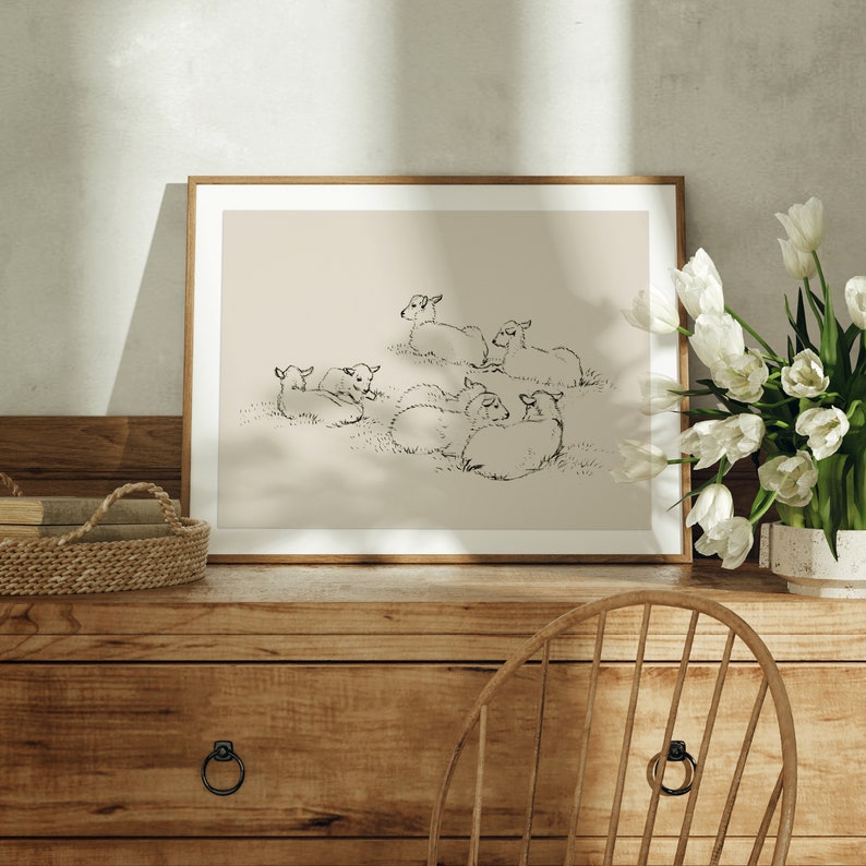 May include: A framed black and white line drawing of a group of sheep lying down in a field. The drawing is on a beige background and is framed in a light wood frame.