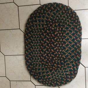 Könnte beinhalten: Ein geflochtener ovaler Teppich mit einem braunen, grünen und roten Muster. Der Teppich ist aus gewebtem Stoff und hat eine strukturierte Oberfläche.